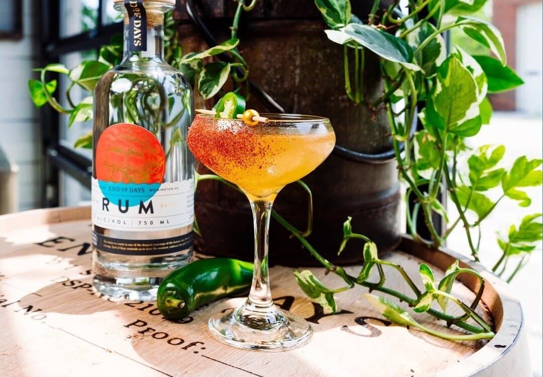 An End of Days rum cocktail with a chili-salt rim beside a bottle of their rum
